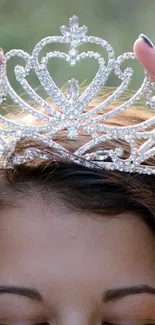 A dazzling silver crown placed gently over a person's head on a mobile wallpaper.