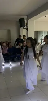 Cultural dance performance in a modern hall with dancers in white attire.