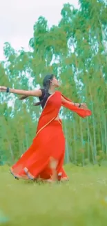 Woman in red saree dancing in a green field.