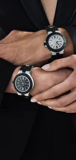 Elegant hands wearing two stylish black watches against a silky black suit background.