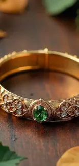 Elegant gold bracelet with emerald stones on a wooden surface.