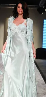 Fashion model in mint green satin gown on runway.