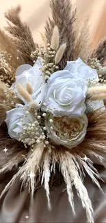 Elegant bouquet of white roses and pampas grass on soft beige fabric.