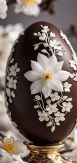 Chocolate egg with white floral designs on a blurred background.