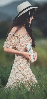 Woman in floral dress and hat in a green field.