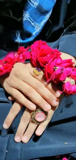 Hand adorned with pink flowers and elegant jewelry against blue fabric.