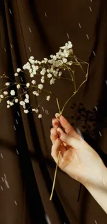 Hand holding white flowers on a brown background mobile wallpaper.