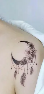 Crescent moon tattoo with flowers and feathers on shoulder.