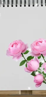 A notebook with pink roses between two potted plants.