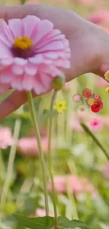 Hand holding pink flower with serene background.