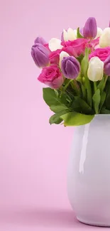 Vibrant bouquet of tulips in white vase on pink background.