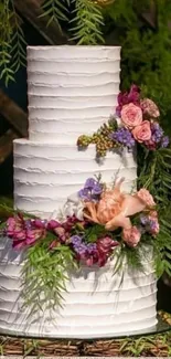 Three-tier white cake with floral decorations and greenery.