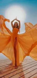 Woman in flowing orange dress under the sun on a wooden deck.