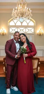 Couple in elegant attire with chandelier and wooden table in background.