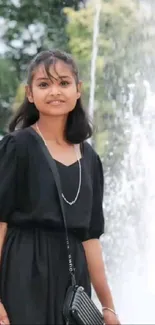 Girl in black dress standing by a fountain.