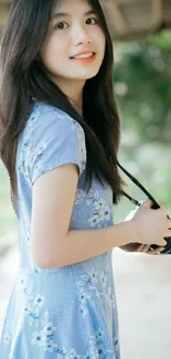 Girl in blue dress holding a camera in natural light.