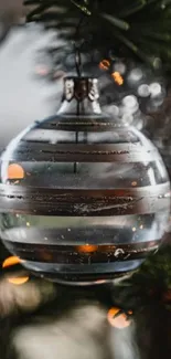 Close-up of a glass Christmas ornament hanging on a green tree branch.