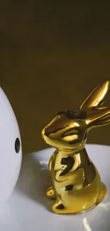 Golden bunny statue beside a polka-dotted egg on a minimalist plate.