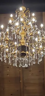 Elegant gold chandelier with crystals against a wooden ceiling.