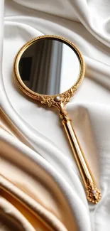 Elegant gold handheld mirror on creamy satin.