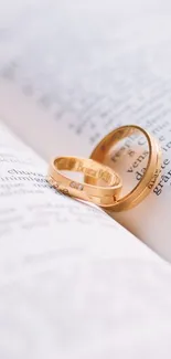 Elegant gold rings on an open book mobile wallpaper.