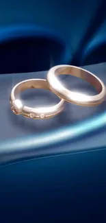 Gold rings intertwined on a silky blue background.