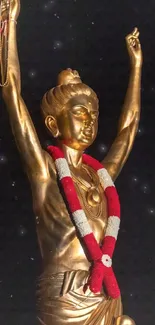 Golden statue with red and white garland on black background.