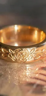 Golden ring with floral engravings on reflective surface wallpaper.