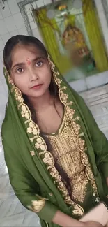 Woman in green traditional attire with gold embroidery and temple background.