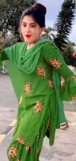 Woman in green dress with floral design outdoors.