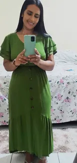 Woman in green dress standing, holding phone.