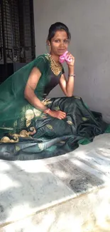 Woman in elegant green saree sitting pose, radiant in light.