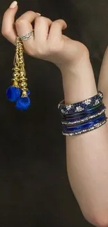 Elegantly adorned hand with blue and gold jewelry on a dark background wallpaper.