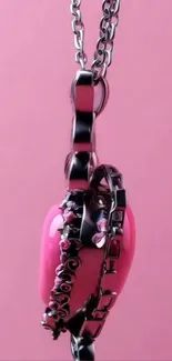 Pink heart pendant with chain on pink background.