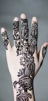 Hand with intricate henna design on beige background.