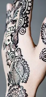 Hand with intricate henna design on gray background.