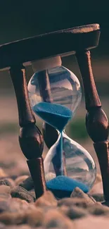 Elegant hourglass with blue sand on pebbles.