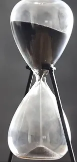 Elegant hourglass with black sand on a dark gray background.