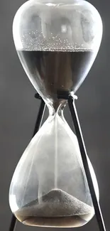 Elegant hourglass with sand on a gray backdrop.