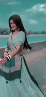 Woman in elegant Indian dress by a serene river with a teal sky.