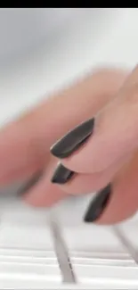 Close-up of hands with black nails typing on a white keyboard.