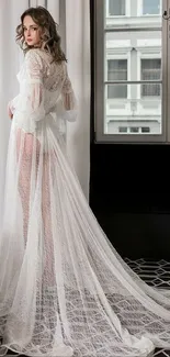 Woman in elegant white lace gown by the window.