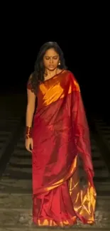 Woman in red saree stands on tracks against dark background.