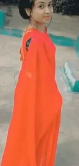 Woman in a vibrant red saree standing elegantly.