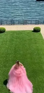 Woman in pink dress by lakeside on green grass.