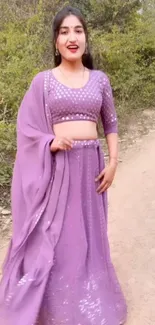 Woman in lavender traditional outfit standing outside with green foliage.