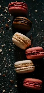 Colorful macarons on dark textured surface.