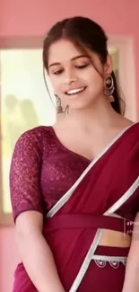 Elegant woman in maroon saree with pink background.