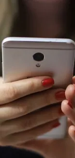 Person holding sleek mobile phone with red nails.