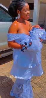 Mother in elegant white dress holding baby outdoors.